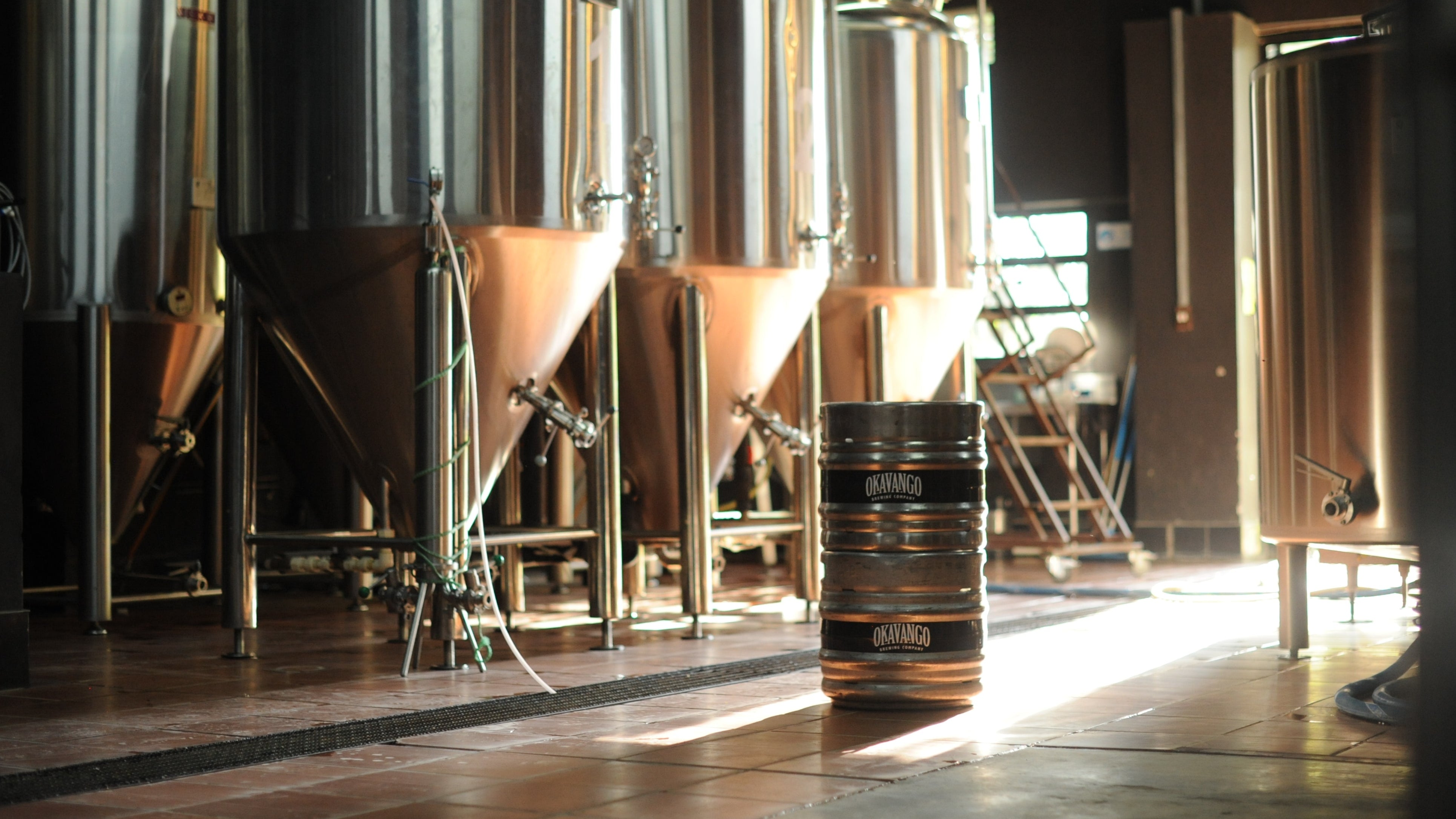 Okavango Brewery interior with large metal tanks and a barrel in the foreground.